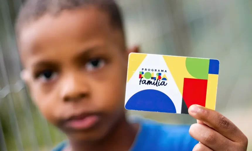 Imagem colorida mostra criança segurando cartão do Bolsa Família