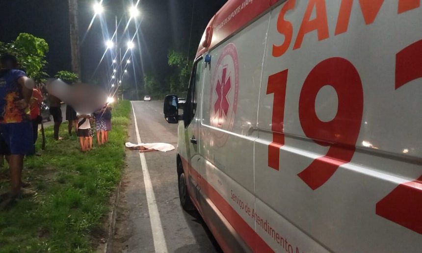 Ambulância do SAMU 192 estacionada em uma estrada, ao lado de um corpo coberto por um lençol branco.