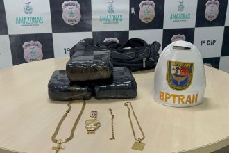 Apreensão de drogas, maconha, em pacotes, além de joias e um boné do BPTran, em cima de uma mesa com o logotipo da Polícia Civil do Amazonas.