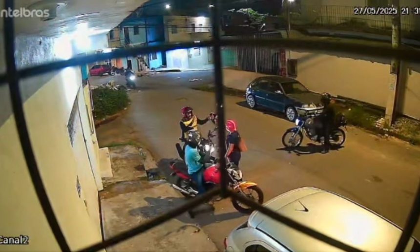 Câmera de segurança mostra dois indivíduos em uma moto sendo abordados por três assaltantes em uma rua à noite.
