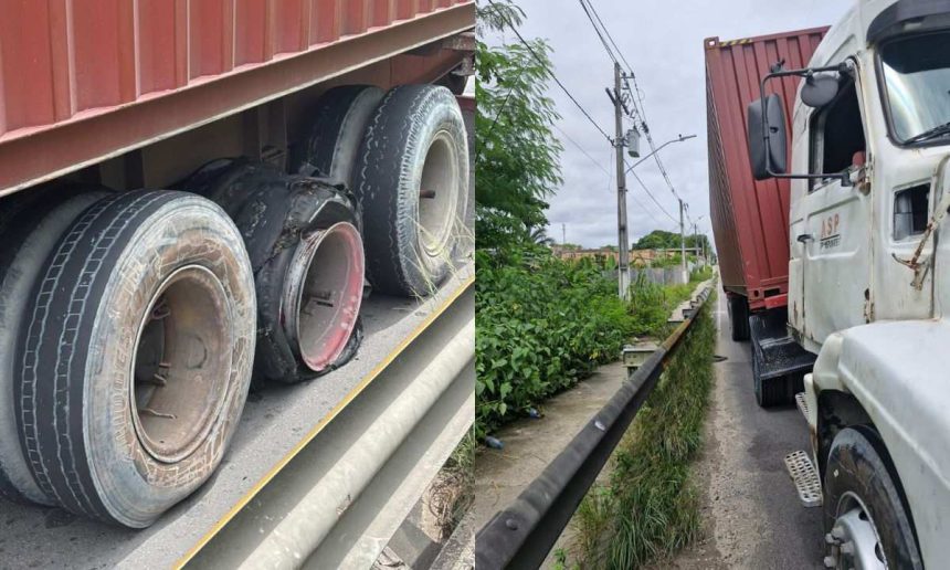 Caminhão com pneus estourados parado na via pública, com um dos pneus completamente desfeito.