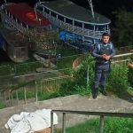 Cena de crime: corpo coberto por um lençol branco em uma escada, policiais e curiosos observam.