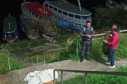 Cena de crime: corpo coberto por um lençol branco em uma escada, policiais e curiosos observam.