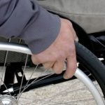 Close-up of a person's hand pushing the wheel of a wheelchair.