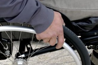 Close-up of a person's hand pushing the wheel of a wheelchair.