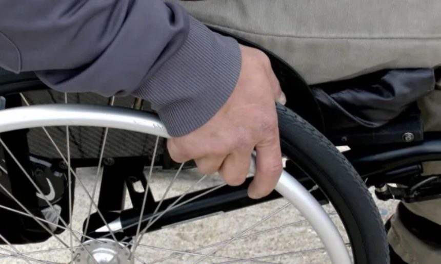 Close-up of a person's hand pushing the wheel of a wheelchair.