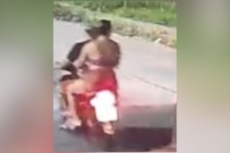 Corpo de uma mulher em uma motocicleta, com um homem atrás dela, ambos mortos. Cena de crime.