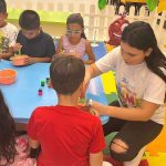 Crianças participando de uma atividade artística com um adulto, com o personagem Stitch do desenho animado Lilo & Stitch, em um ambiente de brinquedoteca no Millennium Shopping.