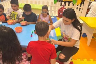 Crianças participando de uma atividade artística com um adulto, com o personagem Stitch do desenho animado Lilo & Stitch, em um ambiente de brinquedoteca no Millennium Shopping.