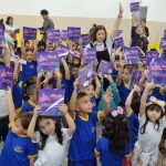 Crianças segurando livros infantis em uma sala de aula. A imagem mostra um grupo de crianças pequenas em uma sala de aula, todas segurando livros infantis e sorrindo para a câmera.