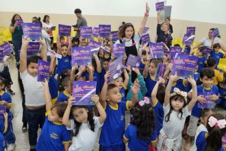 Crianças segurando livros infantis em uma sala de aula. A imagem mostra um grupo de crianças pequenas em uma sala de aula, todas segurando livros infantis e sorrindo para a câmera.