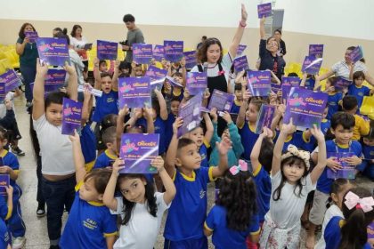 Crianças segurando livros infantis em uma sala de aula. A imagem mostra um grupo de crianças pequenas em uma sala de aula, todas segurando livros infantis e sorrindo para a câmera.