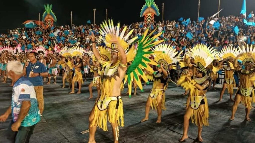 Dançarinos em trajes coloridos se apresentam em um festival em Tabatinga, com uma multidão assistindo ao fundo.