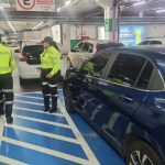 Dois agentes de trânsito autuando um motorista em um estacionamento, por uso irregular de vagas especiais.