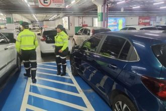 Dois agentes de trânsito autuando um motorista em um estacionamento, por uso irregular de vagas especiais.