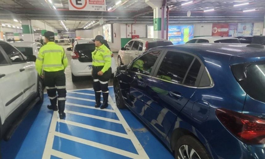 Dois agentes de trânsito autuando um motorista em um estacionamento, por uso irregular de vagas especiais.