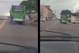 Dois ciclistas andam lado a lado, um deles em frente a um ônibus em movimento, na avenida dos Franceses em Manaus.