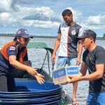 Dois homens entregam uma caixa de água potável para uma mulher em um barco no rio Amazonas, durante enchente.