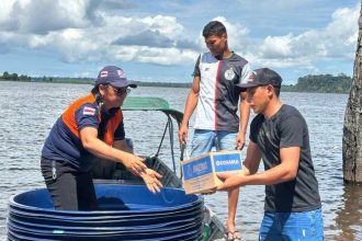 Dois homens entregam uma caixa de água potável para uma mulher em um barco no rio Amazonas, durante enchente.