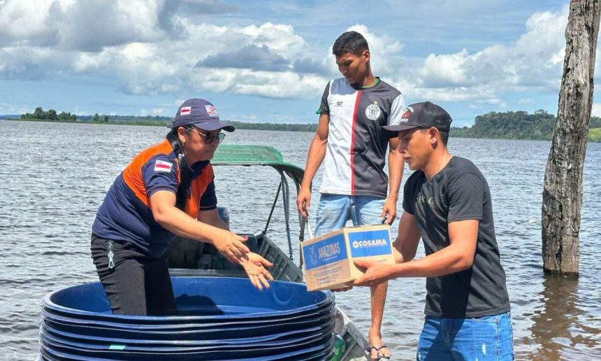 Dois homens entregam uma caixa de água potável para uma mulher em um barco no rio Amazonas, durante enchente.