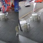 Dois homens retiram uma bandeira do Flamengo de um poste em frente a um bar, com um carro branco estacionado próximo.