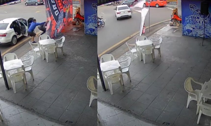 Dois homens retiram uma bandeira do Flamengo de um poste em frente a um bar, com um carro branco estacionado próximo.