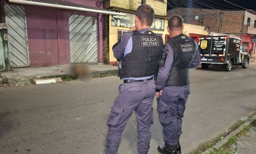 Dois policiais militares em frente a um corpo coberto por um lençol branco, no chão de uma rua, durante um suposto crime.