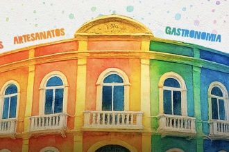 Fachada colorida de um prédio com detalhes em arco, janelas e varandas. A fachada tem o arco decorado com as palavras "Artesanatos", "Gastronomia", "Bebidas" e "Receitas", em destaque.