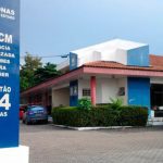 Fachada da Delegacia Especializada em Crimes Contra a Mulher (DECCM) em Manaus, Amazonas, com a placa de plantão 24 horas.