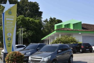 Fachada da Delegacia Especializada em Crimes Contra a Mulher (DECCM) em Manaus, Amazonas, com carros estacionados na frente.