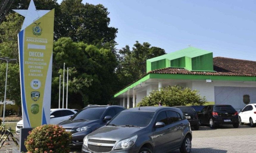 Fachada da Delegacia Especializada em Crimes Contra a Mulher (DECCM) em Manaus, Amazonas, com carros estacionados na frente.