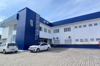 Fachada de um prédio com a inscrição '19ª DP' em destaque, indicando uma delegacia de polícia.