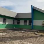 Fachada de uma clínica com paredes verdes e brancas, um estacionamento e um tanque de água alto.