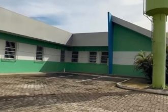 Fachada de uma clínica com paredes verdes e brancas, um estacionamento e um tanque de água alto.