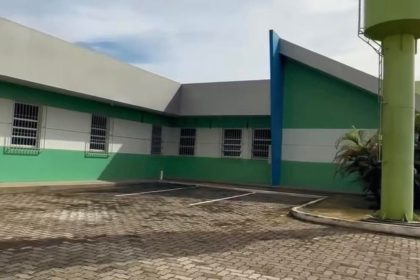 Fachada de uma clínica com paredes verdes e brancas, um estacionamento e um tanque de água alto.