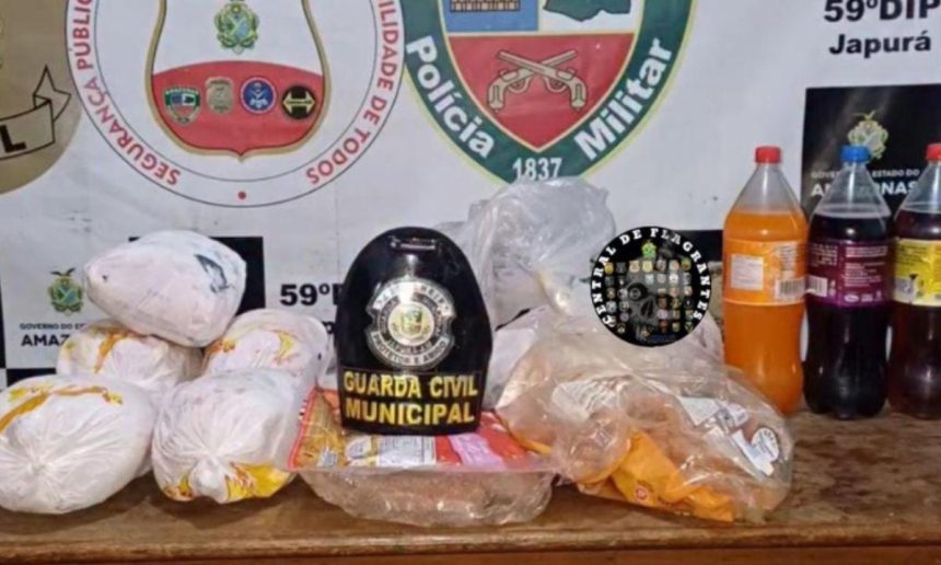 Foto de apreensão de drogas em Japurá, Amazonas. A imagem mostra diversos pacotes de drogas, além de bebidas e um chapéu de guarda civil municipal.