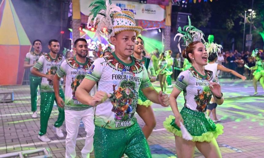 Grupo de dançarinos em trajes coloridos com plumas e fantasias, participando de um evento de festival folclórico, em Manaus.