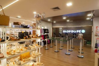 Interior de uma loja de calçados com prateleiras cheias de sapatos, um balcão com a marca 'Shop do Pé' e algumas pessoas.