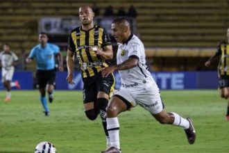 Jogadores de futebol em campo, um em uniforme branco e outro em uniforme listrado amarelo e preto.