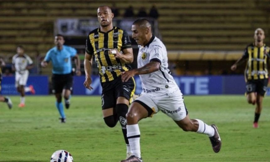 Jogadores de futebol em campo, um em uniforme branco e outro em uniforme listrado amarelo e preto.