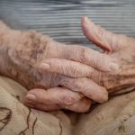 Mãos de uma pessoa idosa juntas em seu colo, com foco nas rugas e marcas do tempo