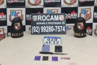 Mesa com objetos apreendidos de suspeitos de roubo, incluindo placa de carro, celular, cartão, faca e símbolo policial.