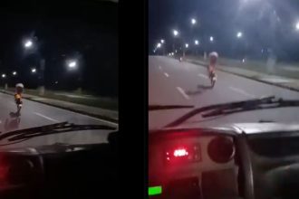 Motociclista em alta velocidade em uma avenida à noite, realizando uma manobra arriscada e perigosa, colocando em risco sua vida e a segurança dos outros motoristas.