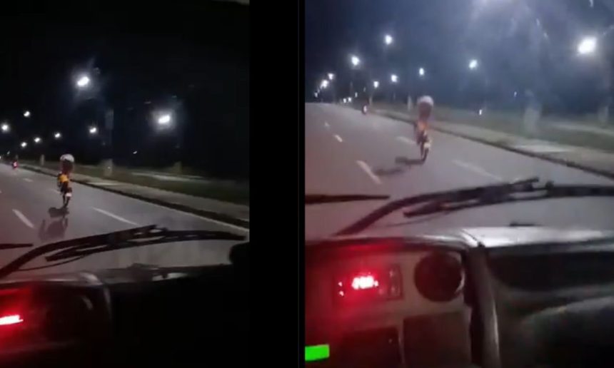 Motociclista em alta velocidade em uma avenida à noite, realizando uma manobra arriscada e perigosa, colocando em risco sua vida e a segurança dos outros motoristas.
