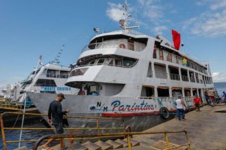 Navio de passageiros atracado no porto de Manaus, com pessoas desembarcando e a escrita "Parintins" visível na lateral, sugerindo viagem para o festival.
