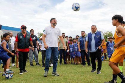 O governador Wilson Lima entrega um estádio modernizado, com crianças jogando bola e autoridades presentes.