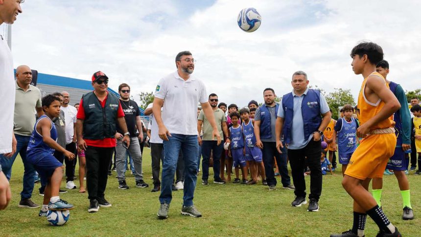 O governador Wilson Lima entrega um estádio modernizado, com crianças jogando bola e autoridades presentes.
