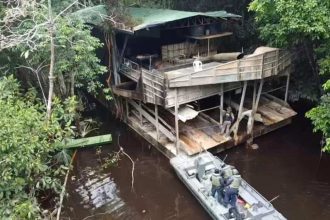 Operação Ágata: Uma embarcação militar próxima a uma estrutura de madeira em um rio, possivelmente em uma área de mata densa.