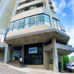 Prédio da CDL Manaus com fachada moderna em tons de cinza e detalhes em azul, localizado em uma rua com árvores e outros edifícios ao fundo.