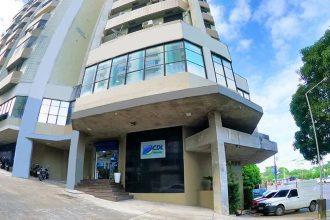 Prédio da CDL Manaus com fachada moderna em tons de cinza e detalhes em azul, localizado em uma rua com árvores e outros edifícios ao fundo.